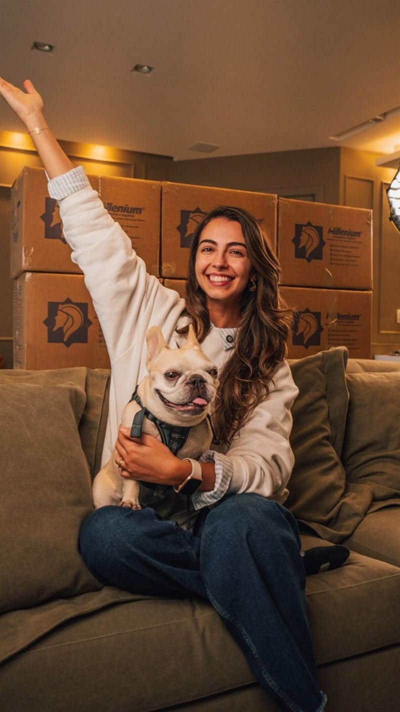 Pessoa comemorando a mudança no sofá com o cachorro no colo, cercada por caixas da Millenium