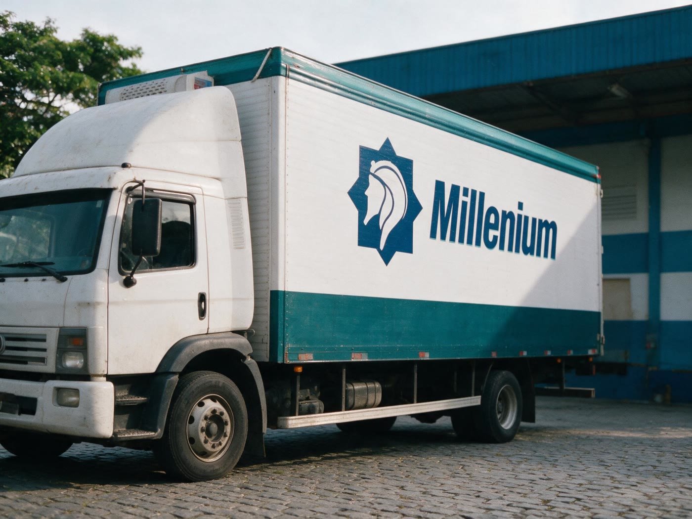 Caminhão baú da frota própria da Millenium Transportes, com a marca aplicada na lateral, estacionado em pátio